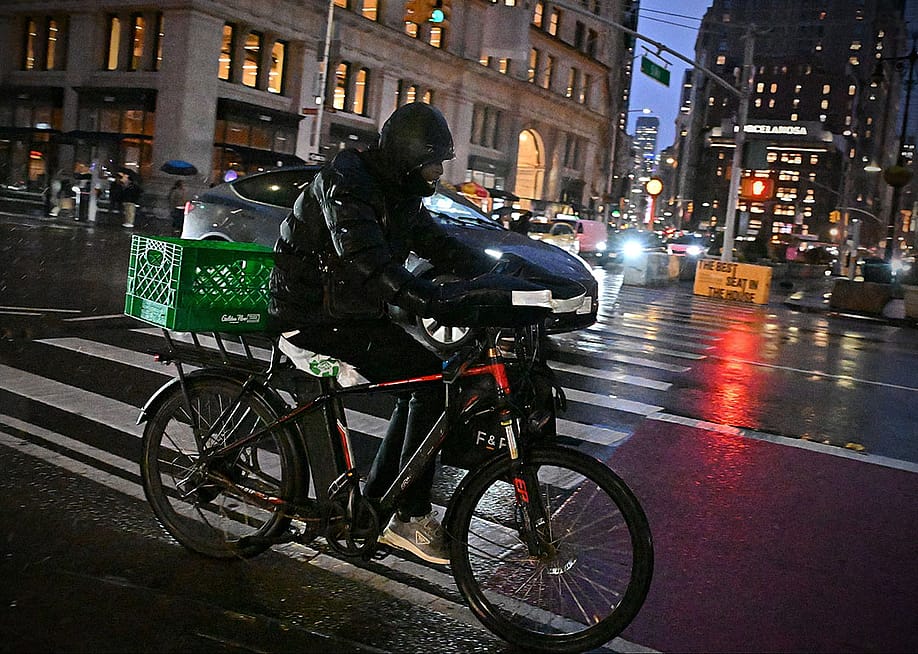 A rider transports a delivery using an e-bike on a street in midtown Manhattan on a rainy night on December 22, 2024 in New York City, USA. — 1000 Words // Shutterstock