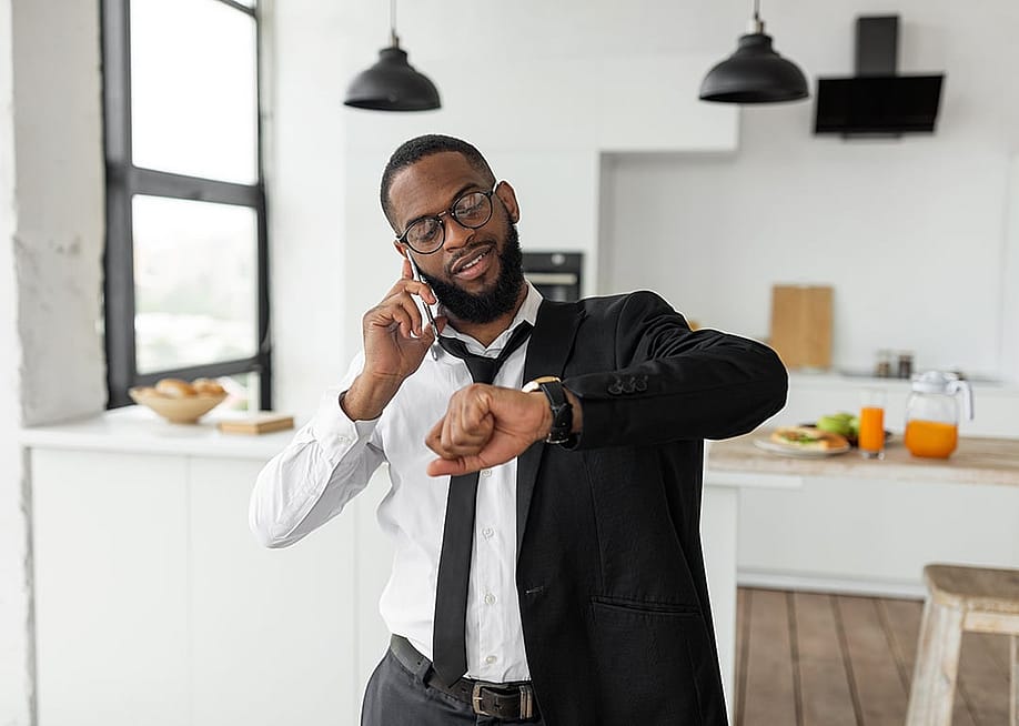 A black businessman on the phone looks at his wrist watch as he gets ready to go to work in the morning. — Prostock-studio // Shutterstock