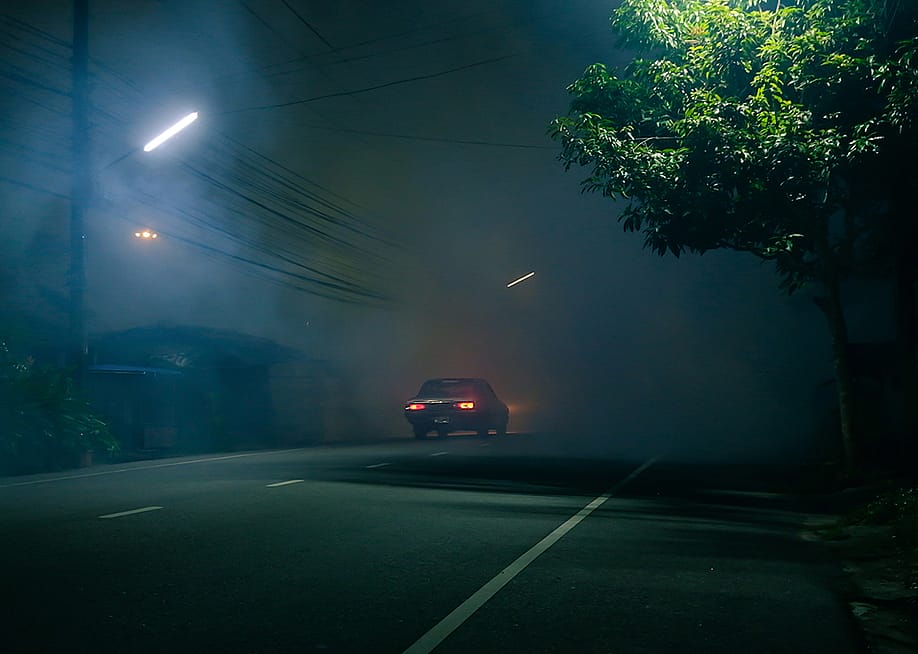 A classic car drives down a spooky road at night. — Apisorn // Shutterstock