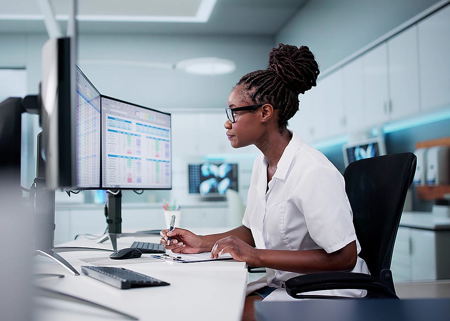 A hospital staff looking at spreadsheets and billing codes using desktop with multiple monitors. — Andrey_Popov // Shutterstock