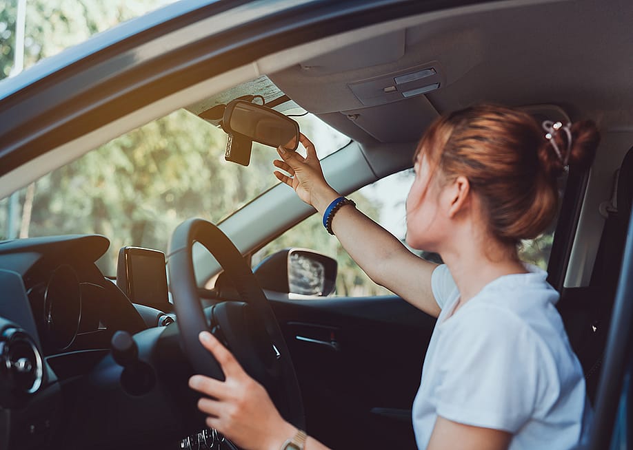 A woman adjusts her car's rearview mirror before driving. — MMD Creative // Shutterstock
