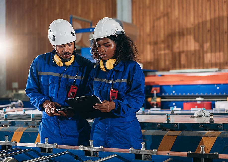 A pair of industrial workers inspect their factory's machines. — NewJadsada // Shutterstock