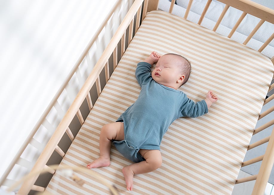 An infant quietly sleeps in a crib. — leungchopan // Shutterstock