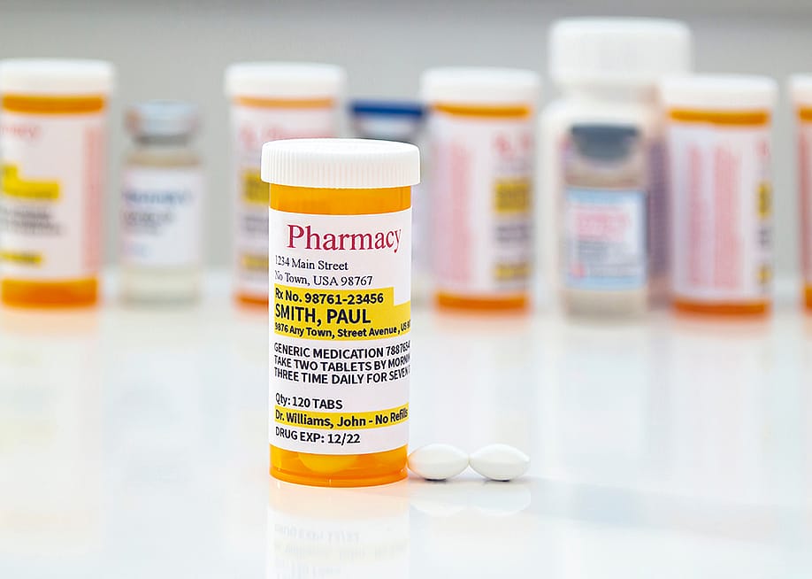 A generic prescription medicine pill bottle in front of a row of other pill bottles. — oasisamuel // Shutterstock