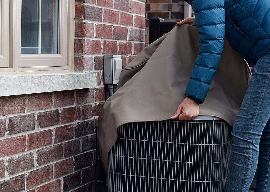 A woman covers their air conditioning unit set outside the house. — JulieK2 // Shutterstock