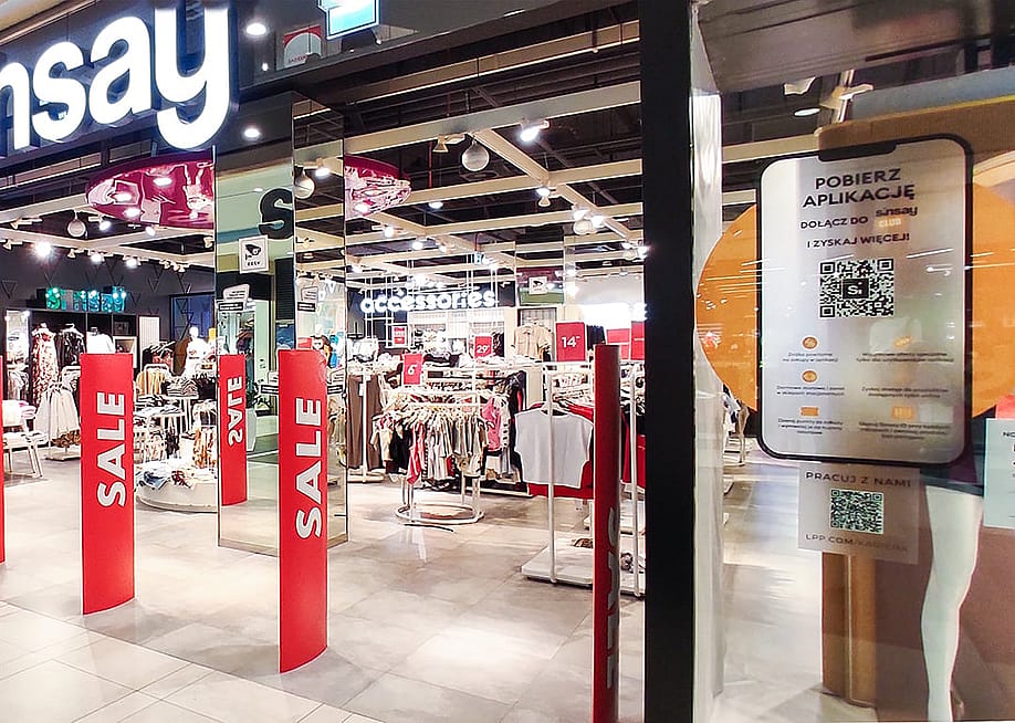 A clothing store having a sale in a shopping mall with a QR code system displayed at the entrance. — Alexa_Space // Shutterstock