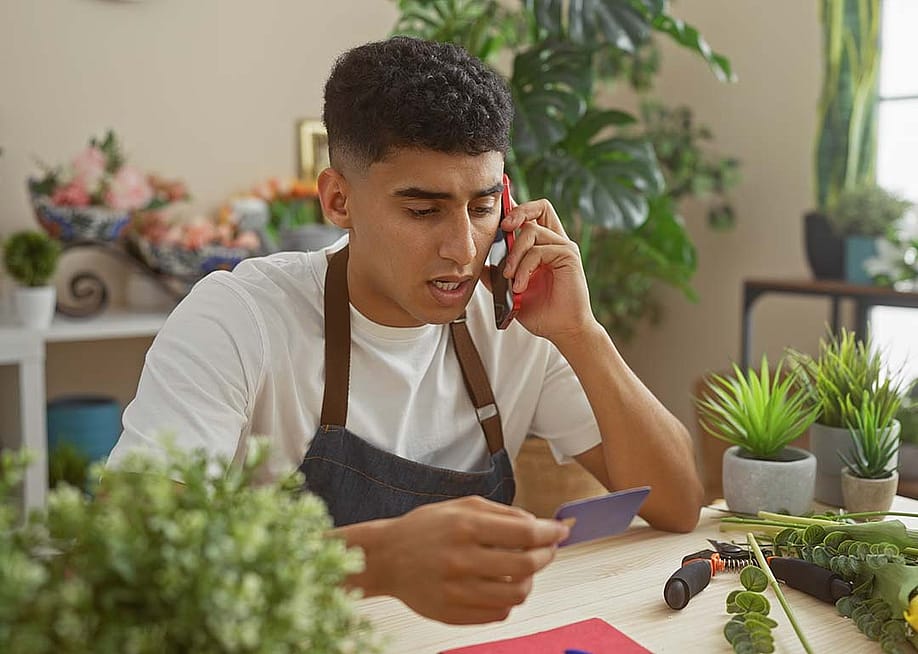 A flower shop business owner holding a credit card while talking on the phone. — Krakenimages.com // Shutterstock