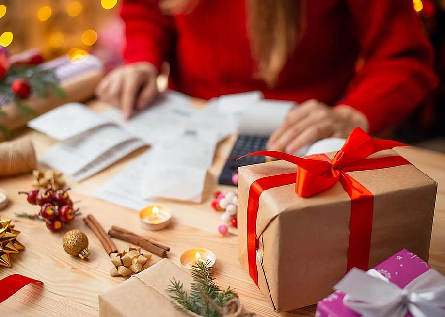 A woman calculates expenses on a table with holiday gifts and decorations. — Vitalii Stock // Shutterstock