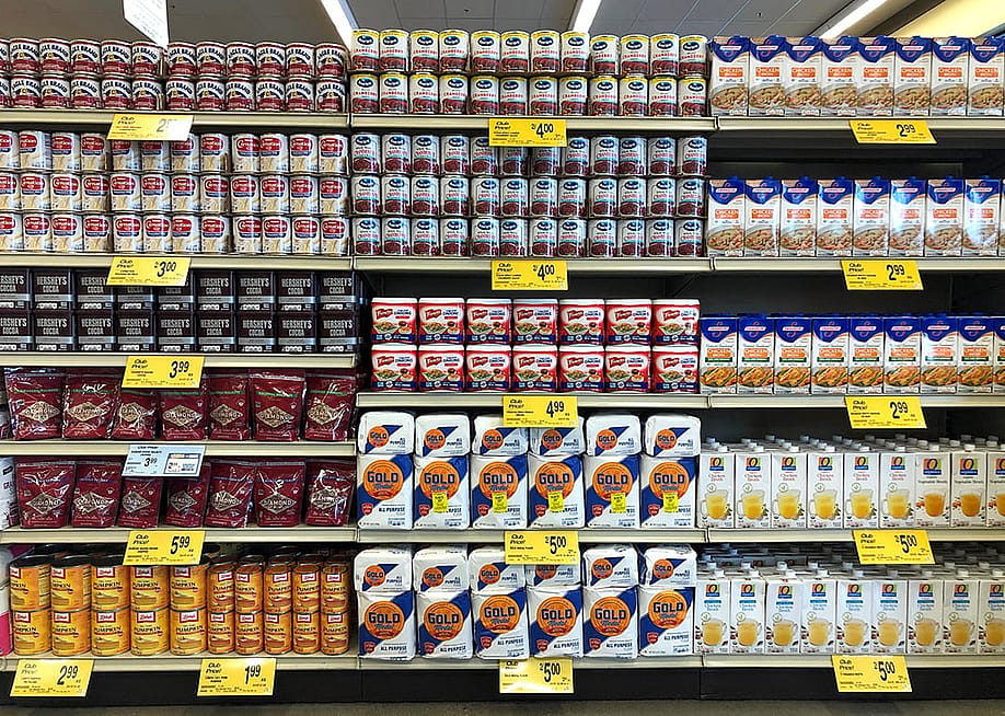 Grocery store shelves of common Thanksgiving and Christmas dinner supplies such as cans of condensed milk, pumpkin puree, and cranberry sauce. — Sheila Fitzgerald // Shutterstock