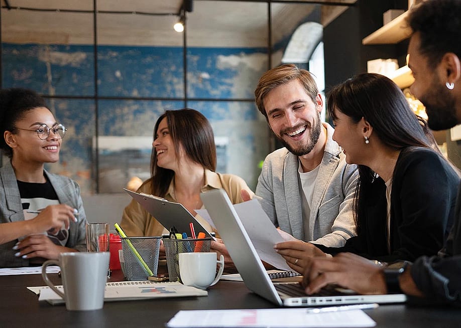 Five members of a business team talking together at a table with laptops open. — OPOLJA // Shutterstock