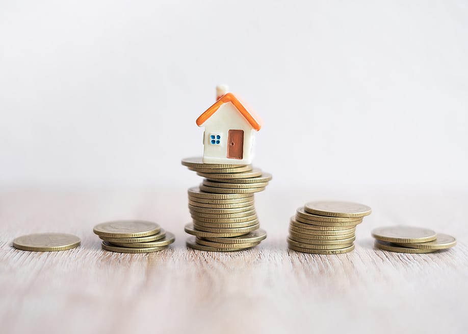 A miniature house on top of a stack of coins. — Kanjana Kawfang // Shutterstock