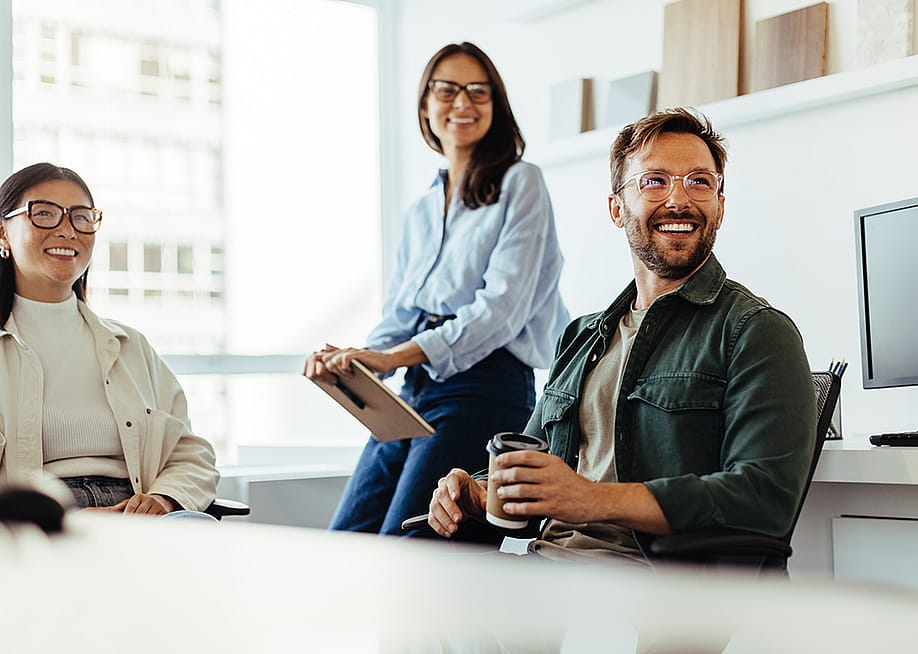 A group of three business people happily listens to a speaker during an office meeting. — JLco Julia Amaral // Shutterstock