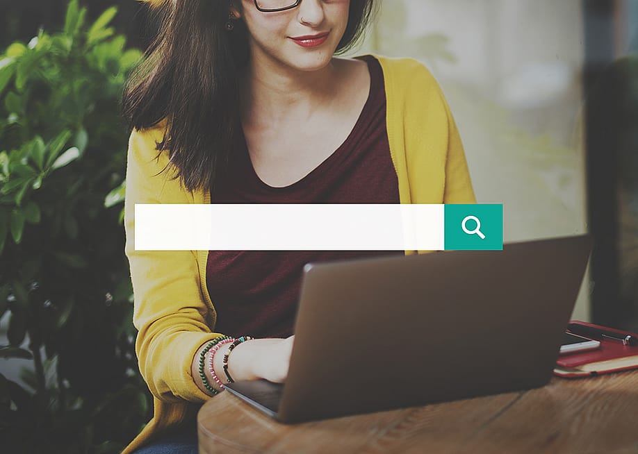 A search bar over a background of a woman using a laptop. — Rawpixel.com // Shutterstock