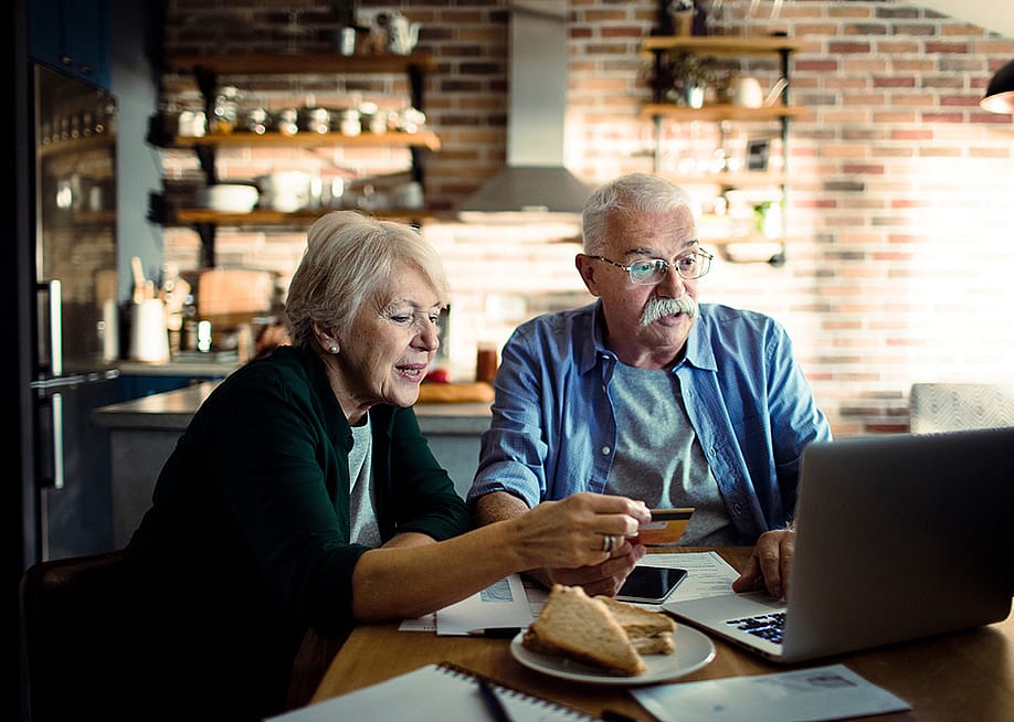 An elderly couple using a credit card at home with a laptop. — Davor Geber // Shutterstock