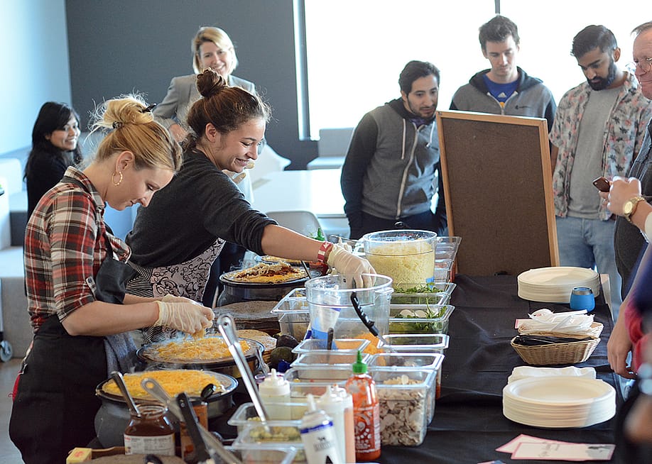 A catering team preparing food in front of awaiting employees. — CaterCow