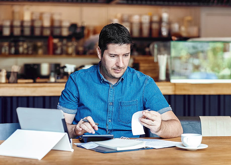 A male restaurant owner calculating business bills. — Dan Rentea // Shutterstock