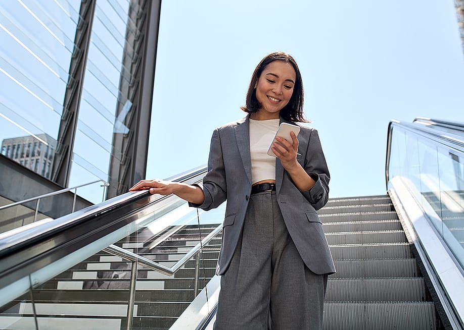 A young female marketing professional smiling at her phone while standing on an escalator. — insta_photos // Shutterstock