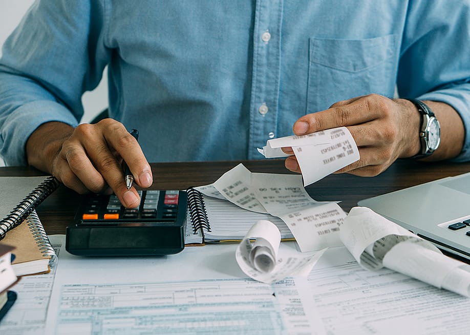 A man computes bills using a calculator. — witsarut sakorn // Shutterstock