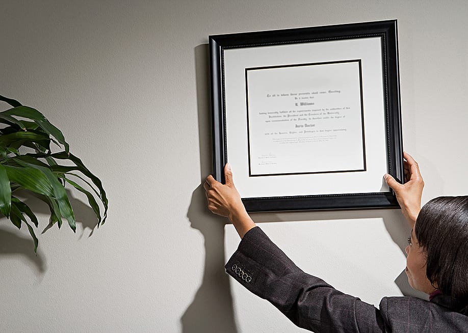 A business woman hanging a framed diploma. — XiXinXing // Shutterstock