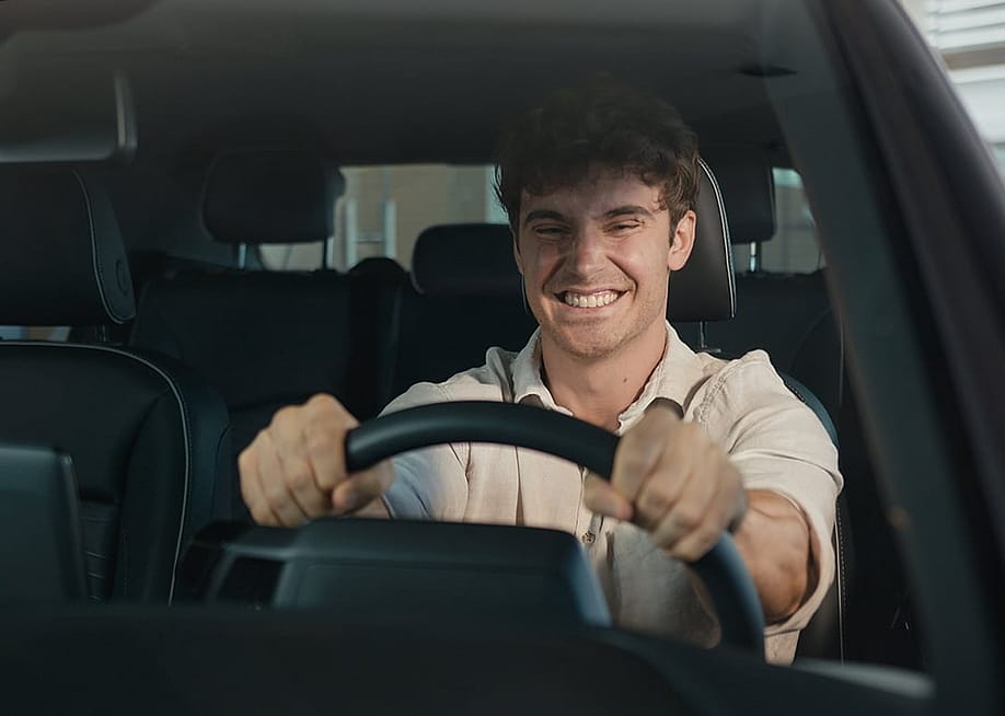 A young man with a big grin sits happily inside a new car. — MAYA LAB // Shutterstock