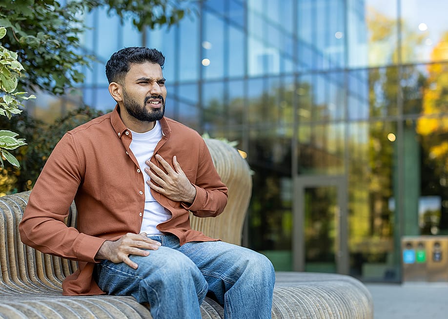 A young man nervously sitting on a bench outdoors experiencing chest pains. — voronaman // Shutterstock
