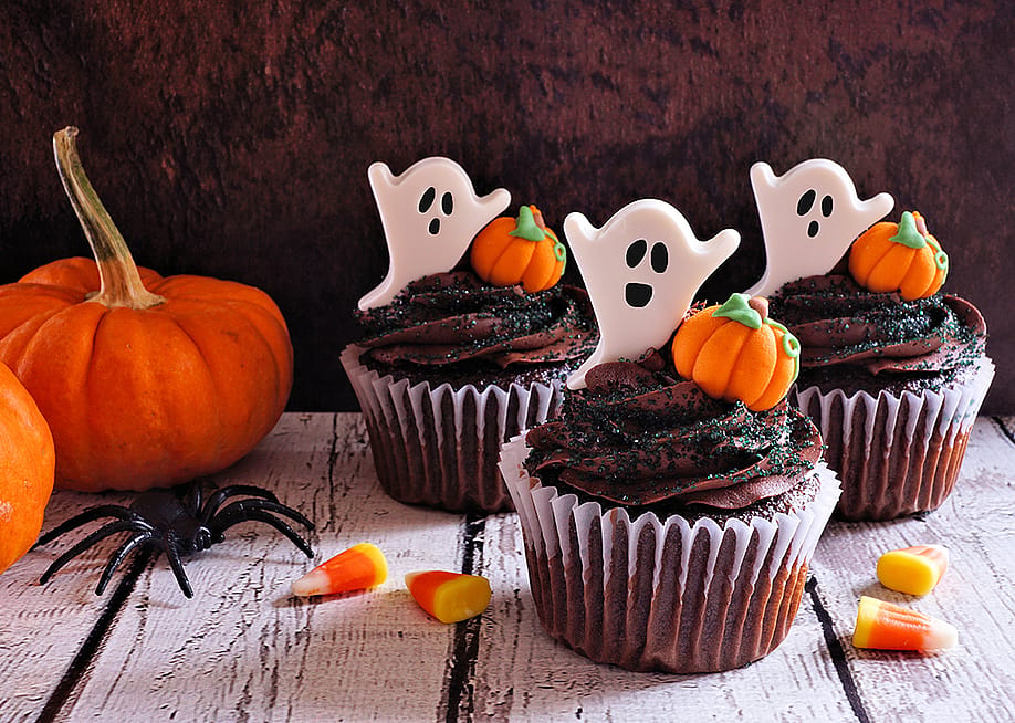 Chocolate cupcakes with ghost toppers beside Halloween pumpkins. — JeniFoto // Shutterstock