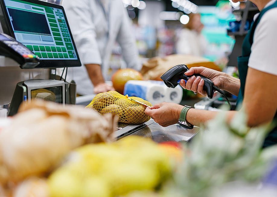 A supermarket cashier staff scans a bag of potatoes at a checkout counter. — Zamrznuti tonovi // Shutterstock