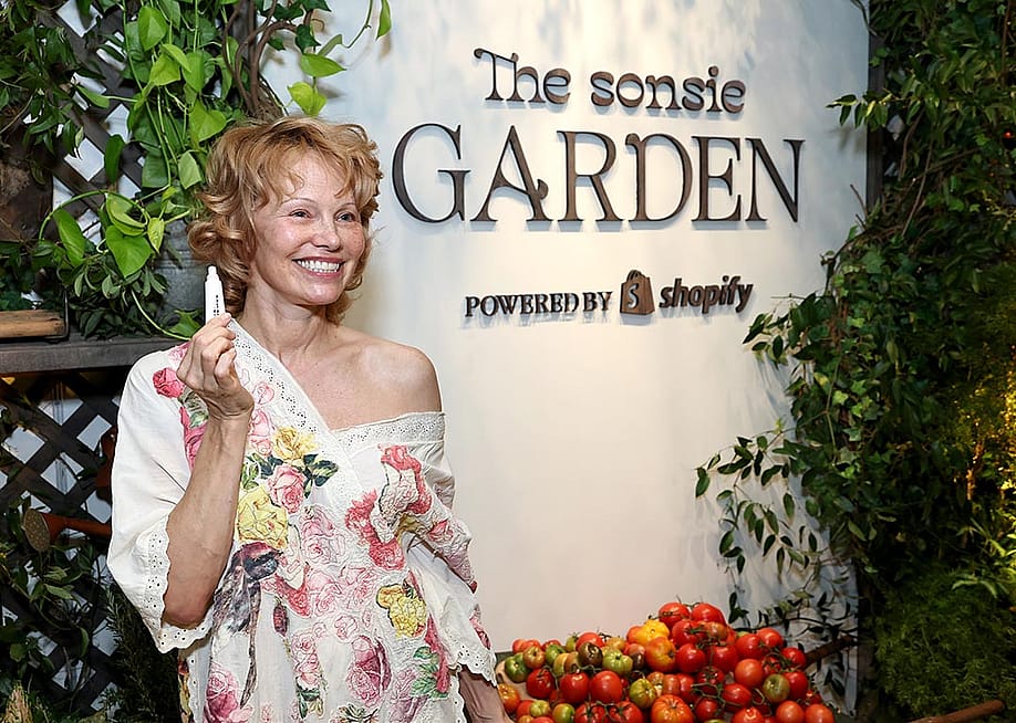 Pamela Anderson poses holding up a lip produce in front of "Sonsie Garden" with Shopify on October 24, 2025 in New York City. — Photo by Jamie McCarthy // Getty Images for Shopify