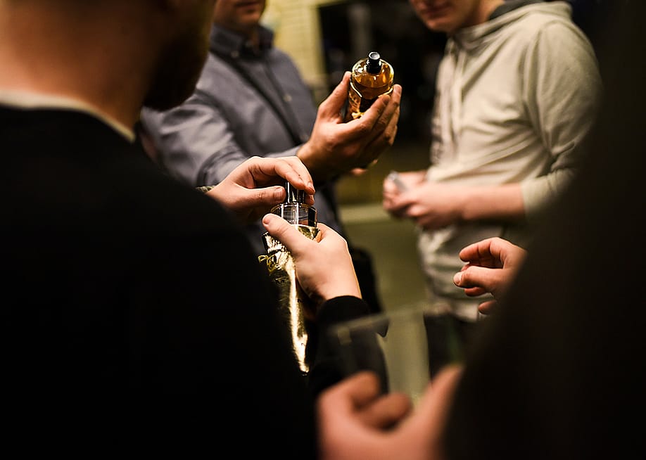 Three men in a room holding perfume bottles and trying out their scents. — DiBeauty // Shutterstock