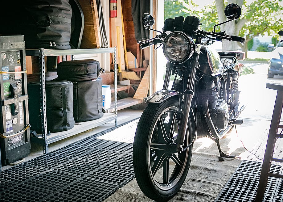 A black vintage motorcycle stored in an open garage. — Benjamin Clapp // Shutterstock