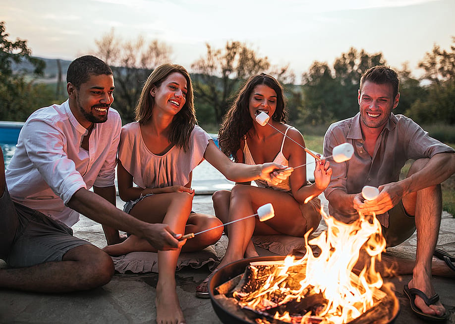 A group of four friends around a campfire grilling s'mores. — bernard // Shutterstock