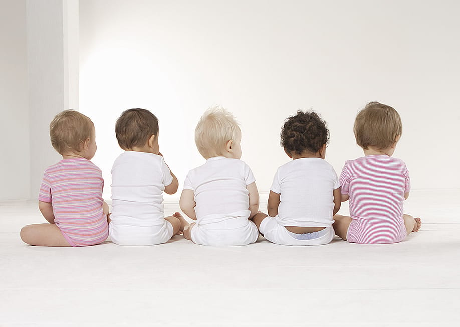 Rear view of five babies sitting on the floor. — Altrendo Images // Shutterstock