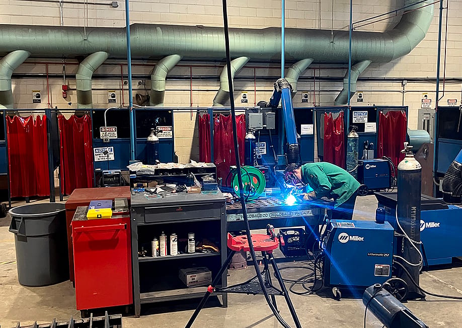 A welding demonstration taking place at a summer program in Philadelphia, colorful stations are in the background. — Carly Sitrin // Chalkbeat