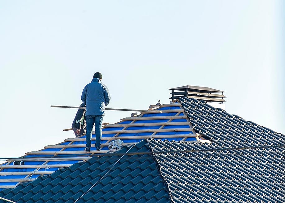 Workers installing metal tile on the roof while roofing house in construction site. — Serhii Krot // Shutterstock
