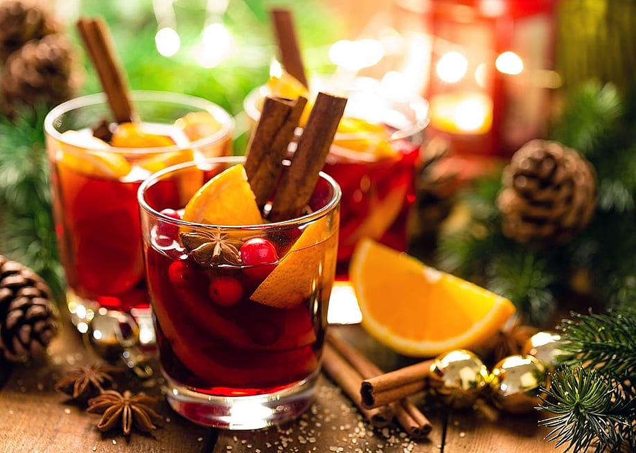 Christmas mulled red wine with spices and oranges on a wooden rustic table with evergreen decor and pine cones in the background. — Sea Wave // Shutterstock