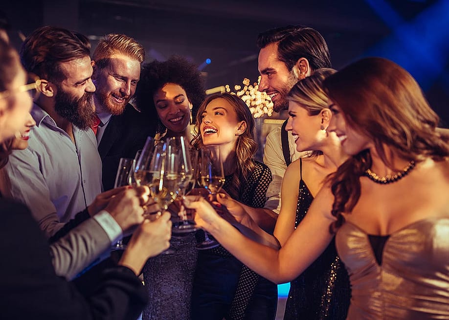 A group of people in party dresses and suits clink glasses together in a party setting. — bbernard // Shutterstock