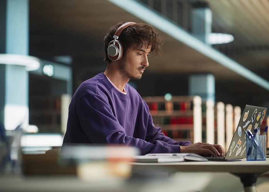Person wearing purple sweatshirt and phones working on laptop in library. — Gorodenkoff // Shutterstock