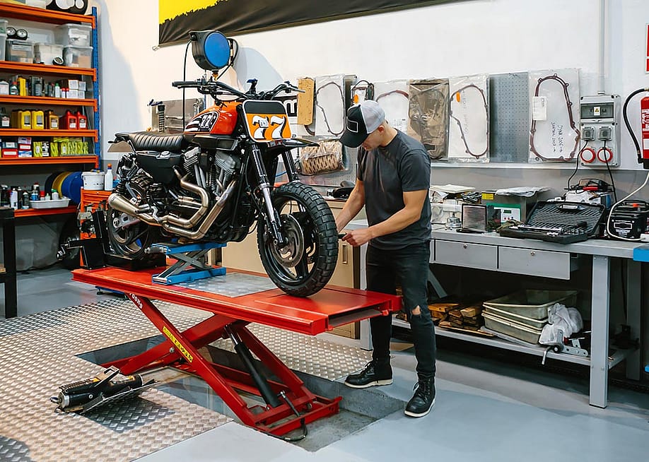 Unrecognizable mechanic man checking engine of custom motorcycle over platform. — David Pereiras // Shutterstock