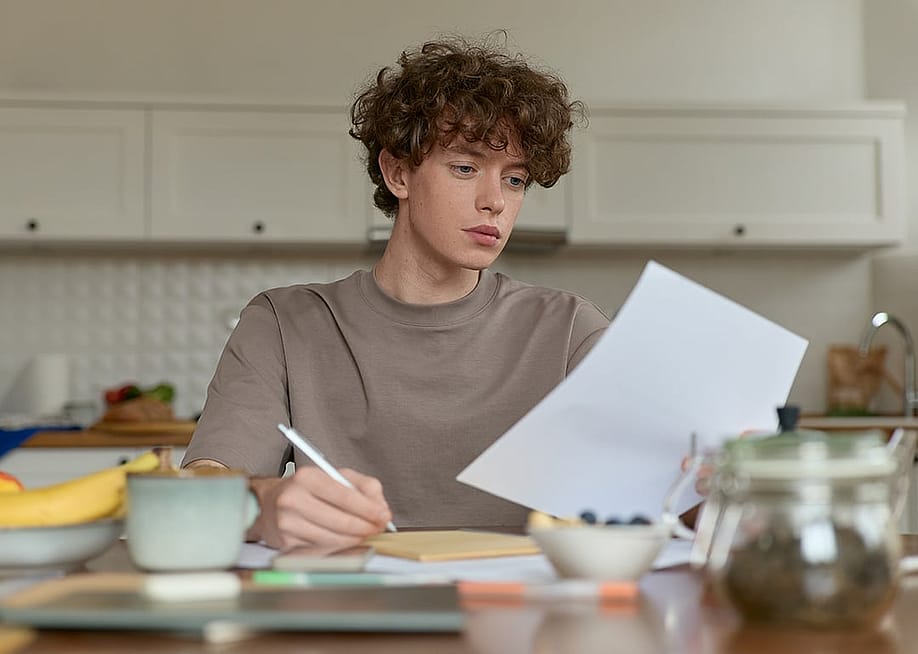 A young man reviewing a document during breakfast. — Folenial // Shutterstock