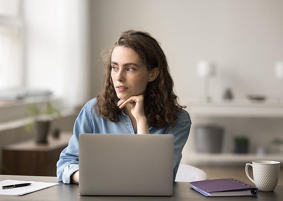 Woman sits at desk with open laptop computer, looking into the distance. — fizkes // Shutterstock