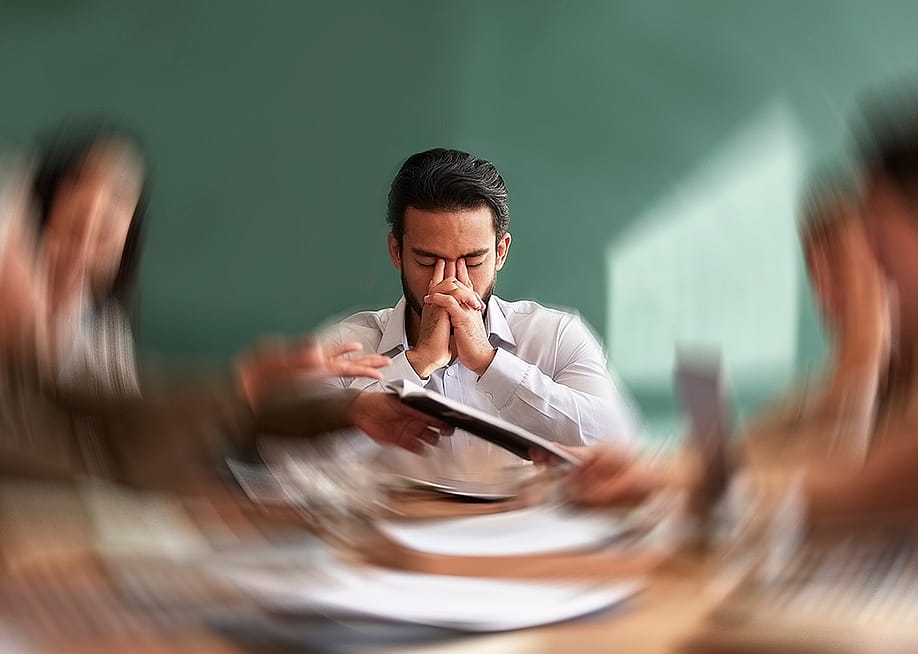 A male employee seated at the center of an office table with his surroundings are illustrated with a motion blur. — PeopleImages // Shutterstock