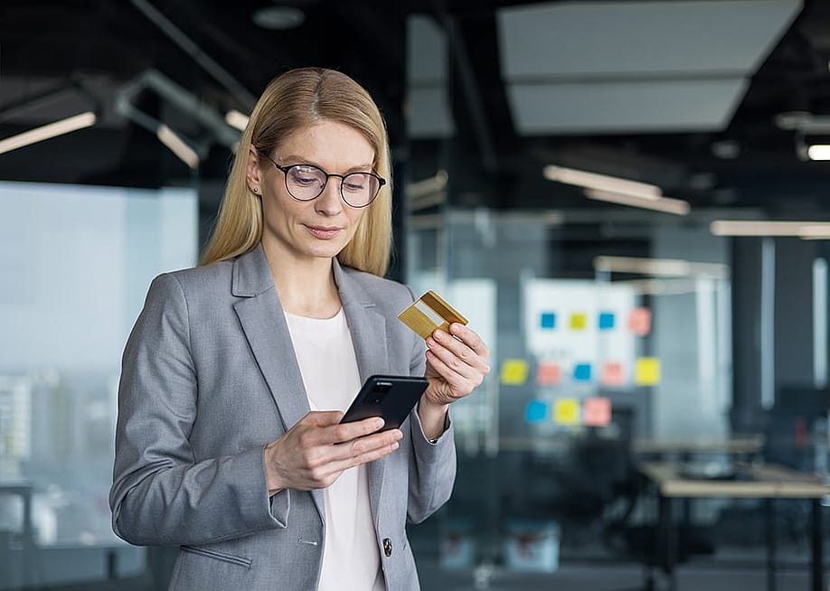 A businesswoman holding a phone and a credit card in an office. — voronaman // Shutterstock