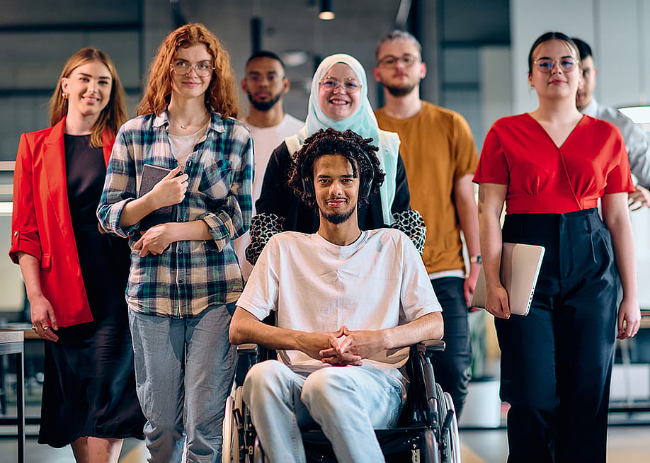 A diverse group of young business people, with a person in wheelchair at the center, showcasing community and accessibility. — dotshock // Shutterstock