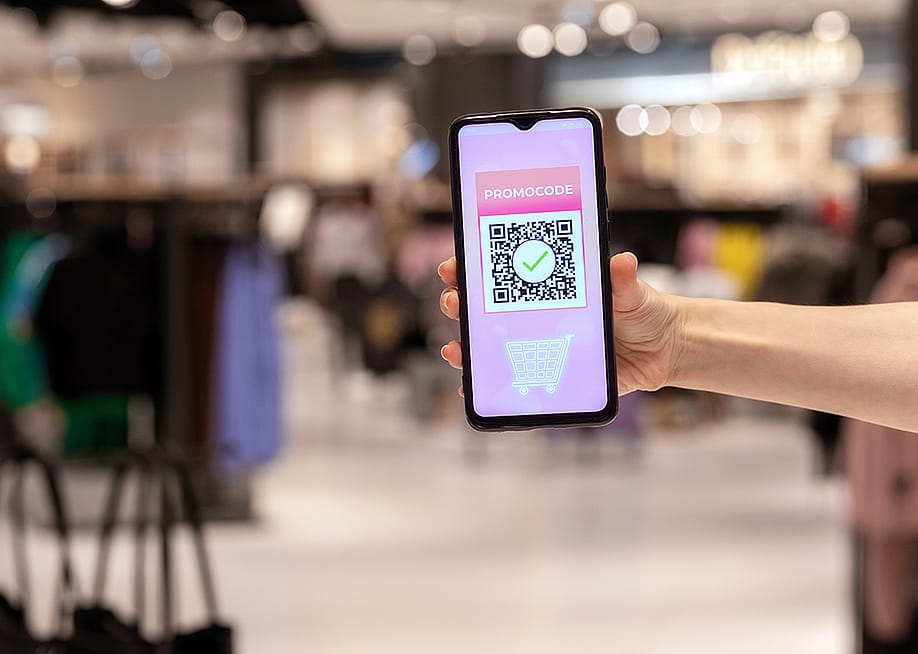 A woman's hand holding a phone displaying promo code applied by scanning a QR code inside a shopping mall. — STEKLO // Shutterstock