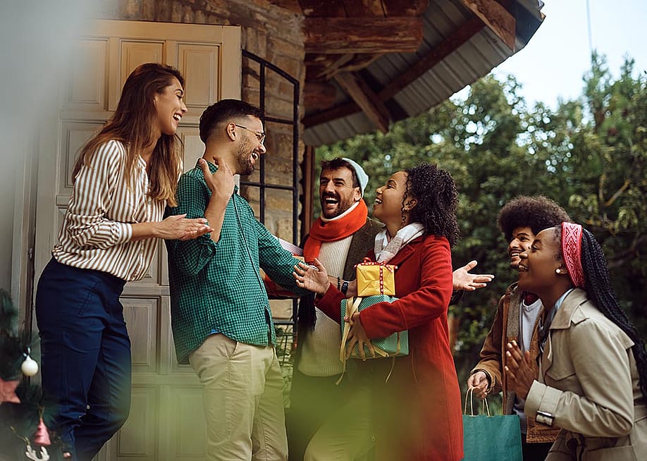 Young happy people greeting with a couple while arriving at their dinner party during winter holidays. — Drazen Zigic // Shutterstock