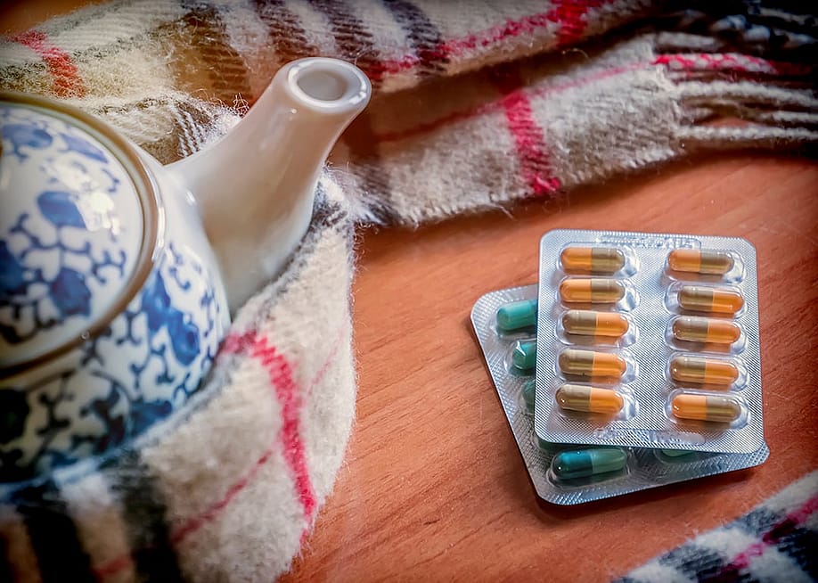 Sheets of pills beside a teapot wrapped in scarf. — digicomphoto // Shutterstock