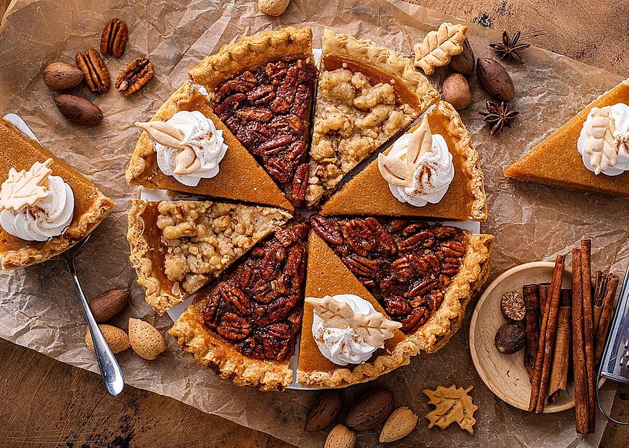 A pie composed of alternating slices of pumpkin with whipped cream and pecan pie, on parchment paper. — Elena Veselova // Shutterstock