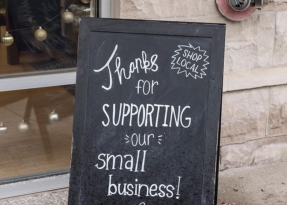 Small business chalkboard sign on sidewalk saying "Thanks for supporting our small business." — CiEll // Shutterstock.