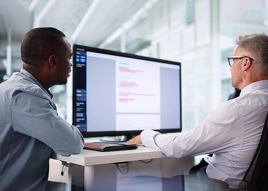 Two people sitting at a desk looking at a large screen; one is a privacy compliance specialist ensuring HIPAA regulations are being followed correctly. — Andrey_Popov // Shutterstock