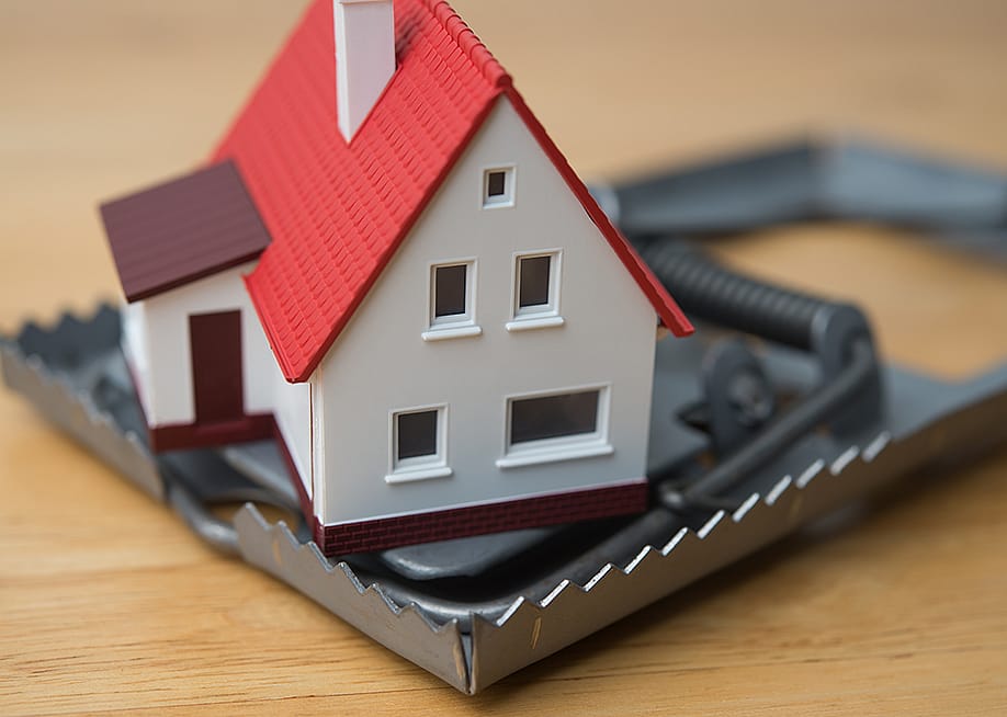 Mortgage scam concept depicted by a figure of a house inside a steel trap. — Pla2na // Shutterstock